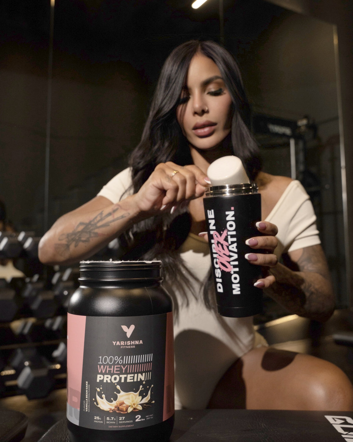 Yarishna Ayala adding a scoop of 100% Whey Protein Vanilla Bean Cake to her shaker at the gym